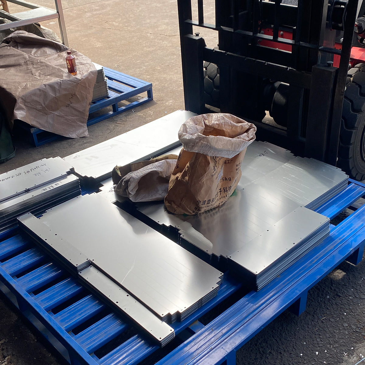 Large batch of laser-cut sheet metal panels stacked on workshop pallets
