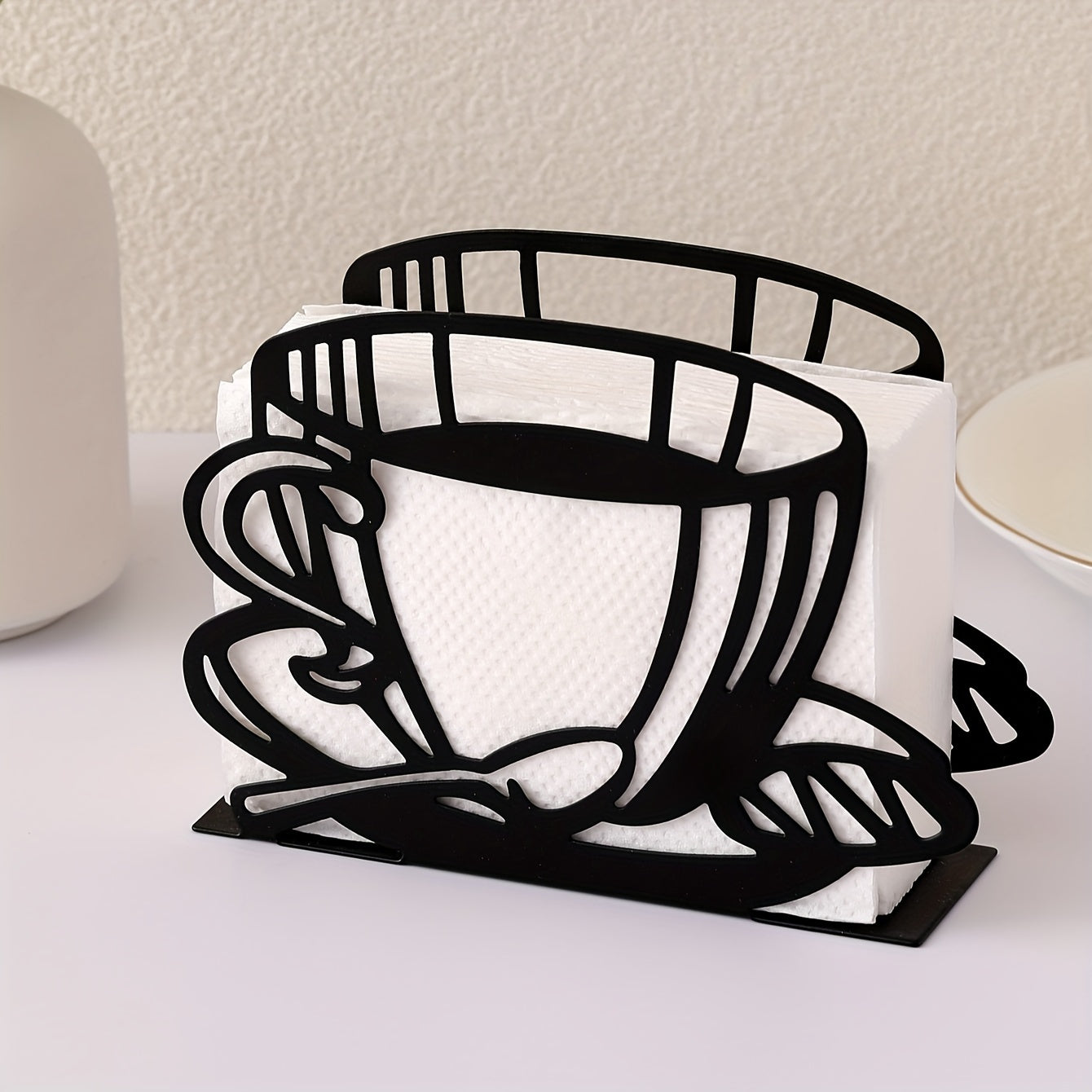 Black metal coffee cup napkin holder filled with white paper napkins