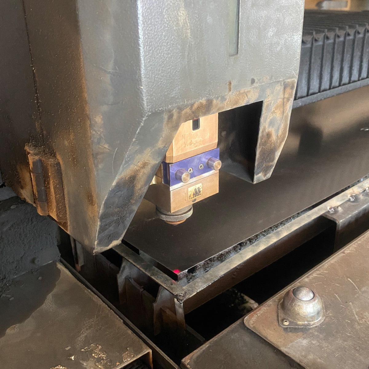 Close-up of a fiber laser cutting head positioned above a sheet metal panel