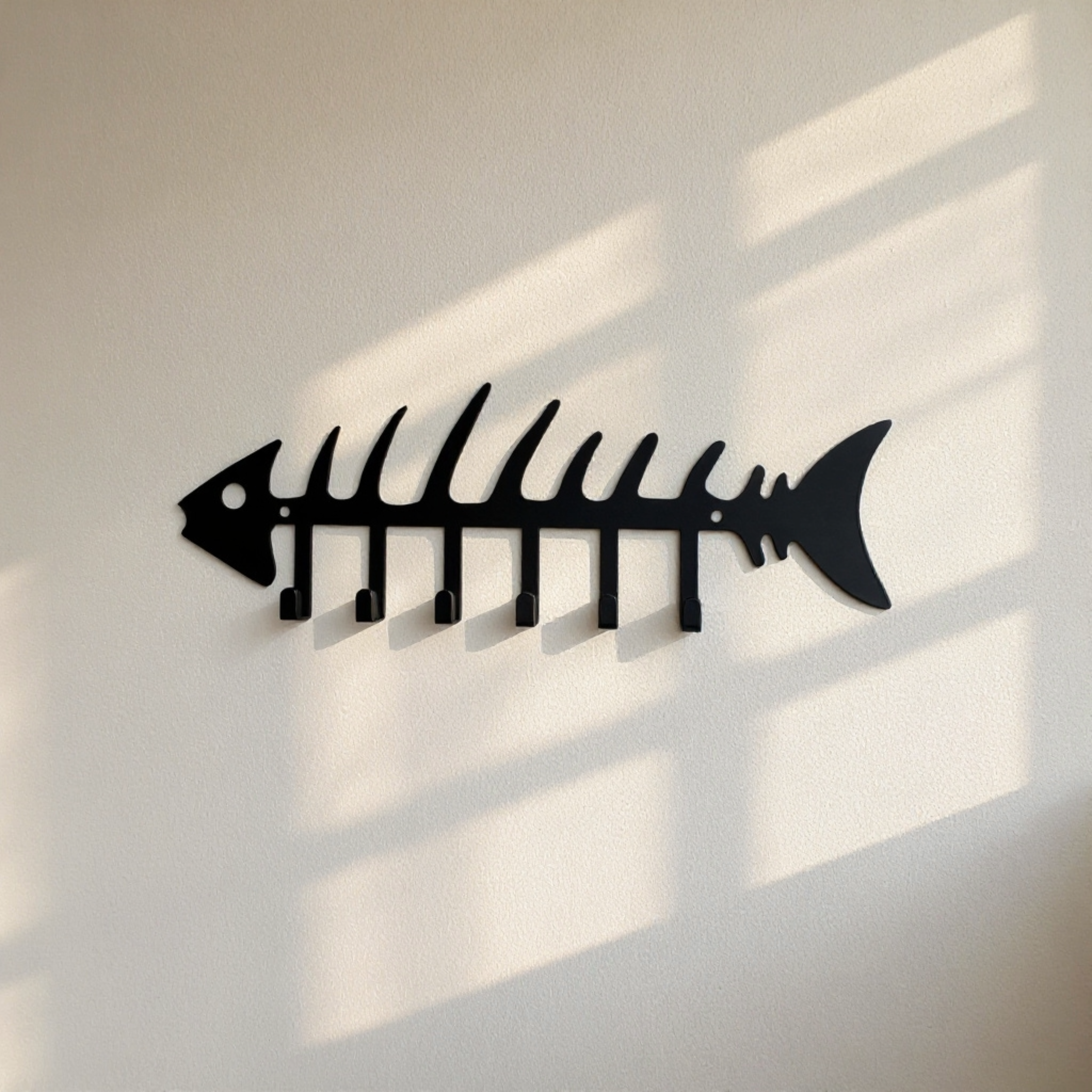 Black metal fishbone wall hook rack with multiple hooks displayed on a wall