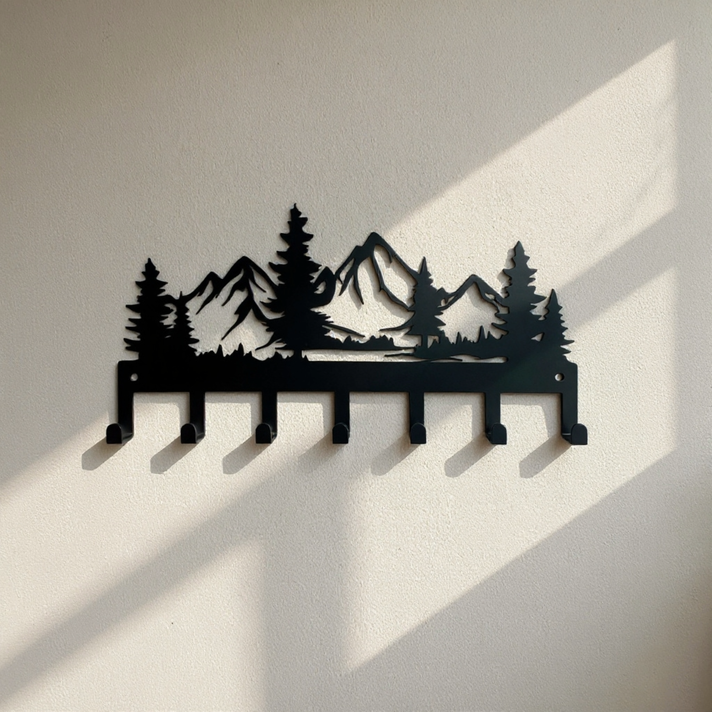 Black metal wall hook rack with a mountain and pine forest design