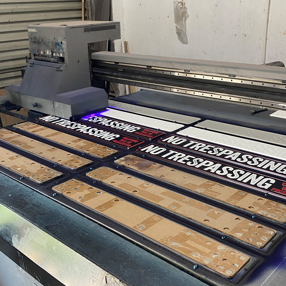 UV printer producing a batch of custom no trespassing metal signs in our workshop