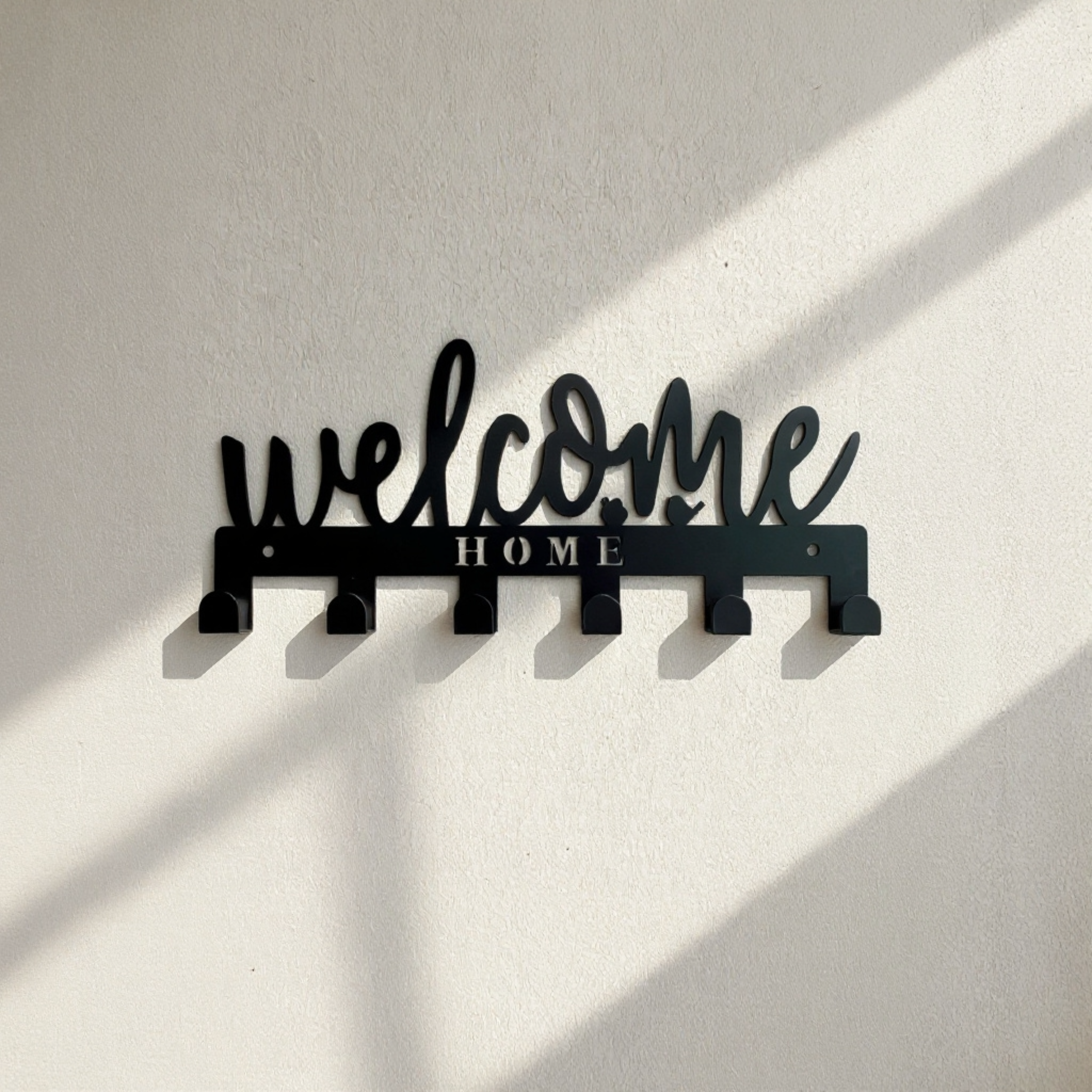 Black metal Welcome Home wall hook rack with six hooks mounted on a wall